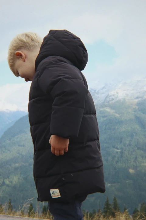 Konges Sløjd Alpi Long Black – czarna kurtka zimowa noszona na tle górskiego krajobrazu