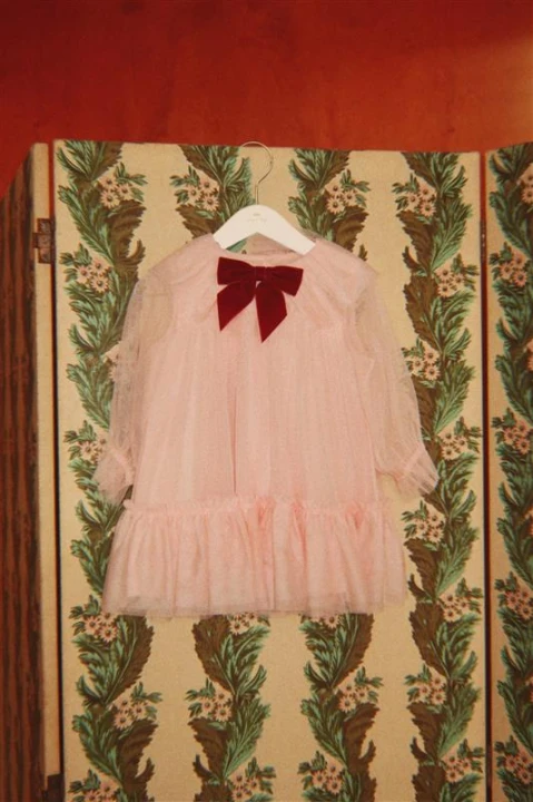 Konges Sløjd Bow Dress Creole Pink – tiulowa sukienka z kokardą na tle dekoracyjnej aranżacji.