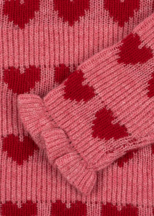 Sweter Laula Konges Sløjd – zbliżenie na rękaw z falbanką przy mankiecie, na tle dzianiny w czerwone serca.