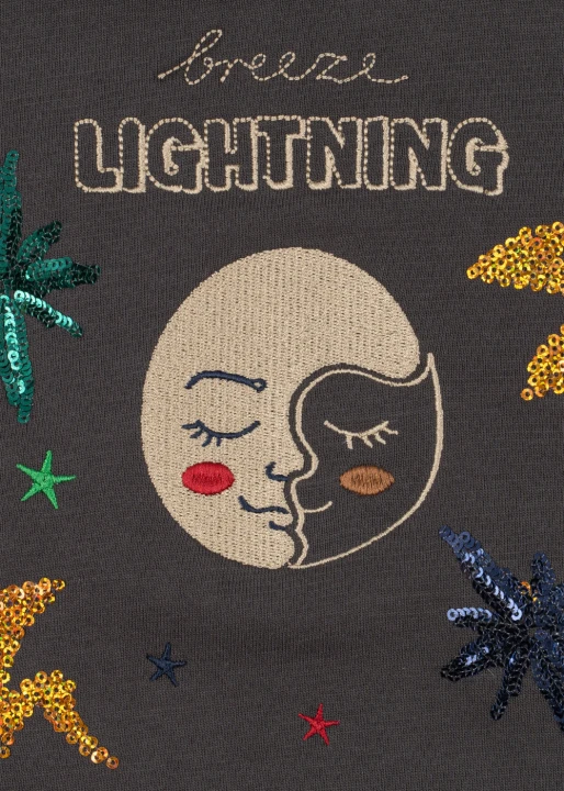 Grafika na bluzie Loupy Lou Magnet – zbliżenie na księżyc z twarzą oraz kolorowe gwiazdy i błyszczące motywy wokół niego.