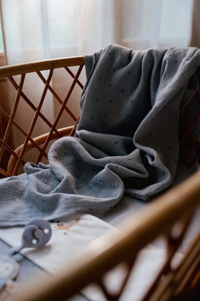 Otulacz muślinowy niebieski w delikatne listki w łóżeczku