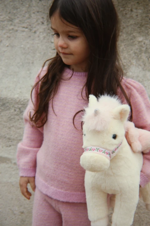 Konges Sløjd Starlight Unicorn Off White pluszak trzymany przez dziewczynkę
